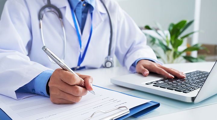 Doctor checking information in computer program before filling medical card